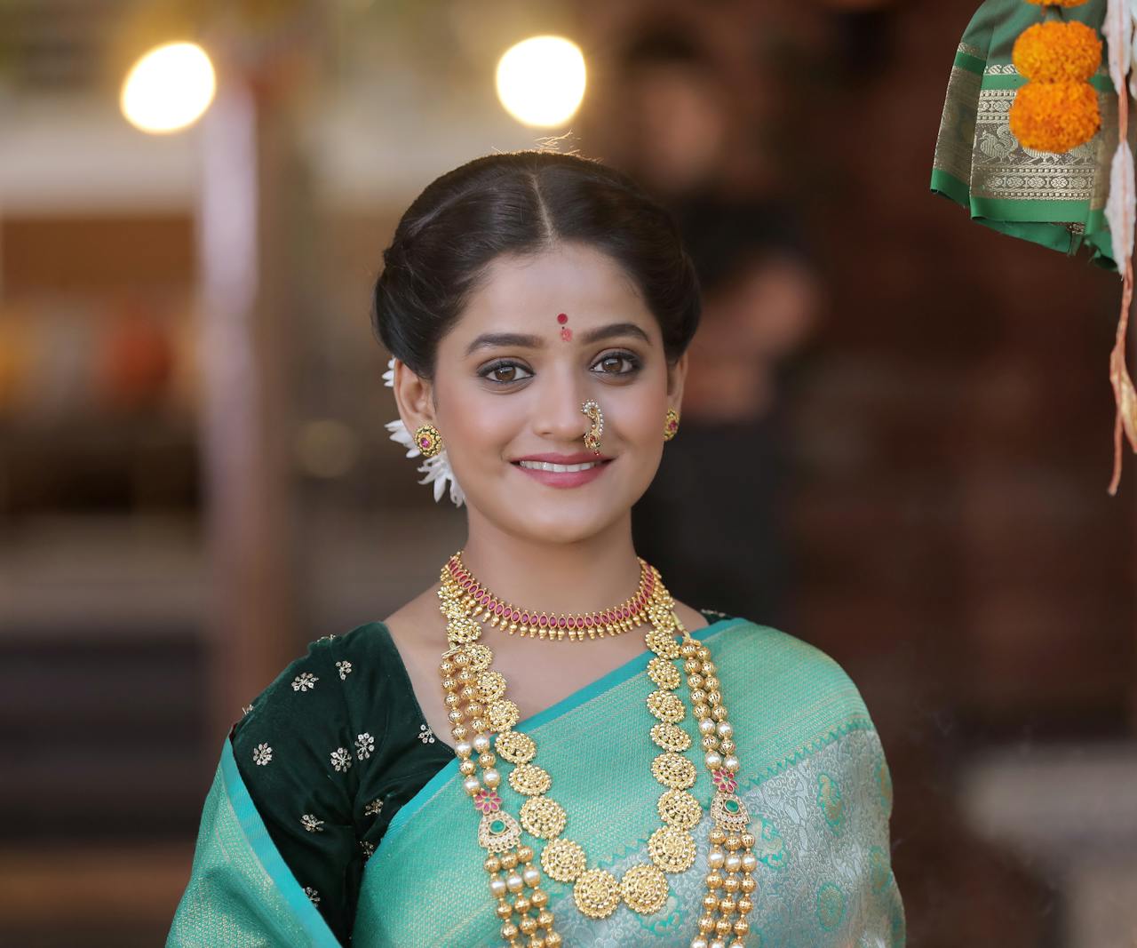 Elegant Indian woman in traditional attire with jewelry, smiling indoors.